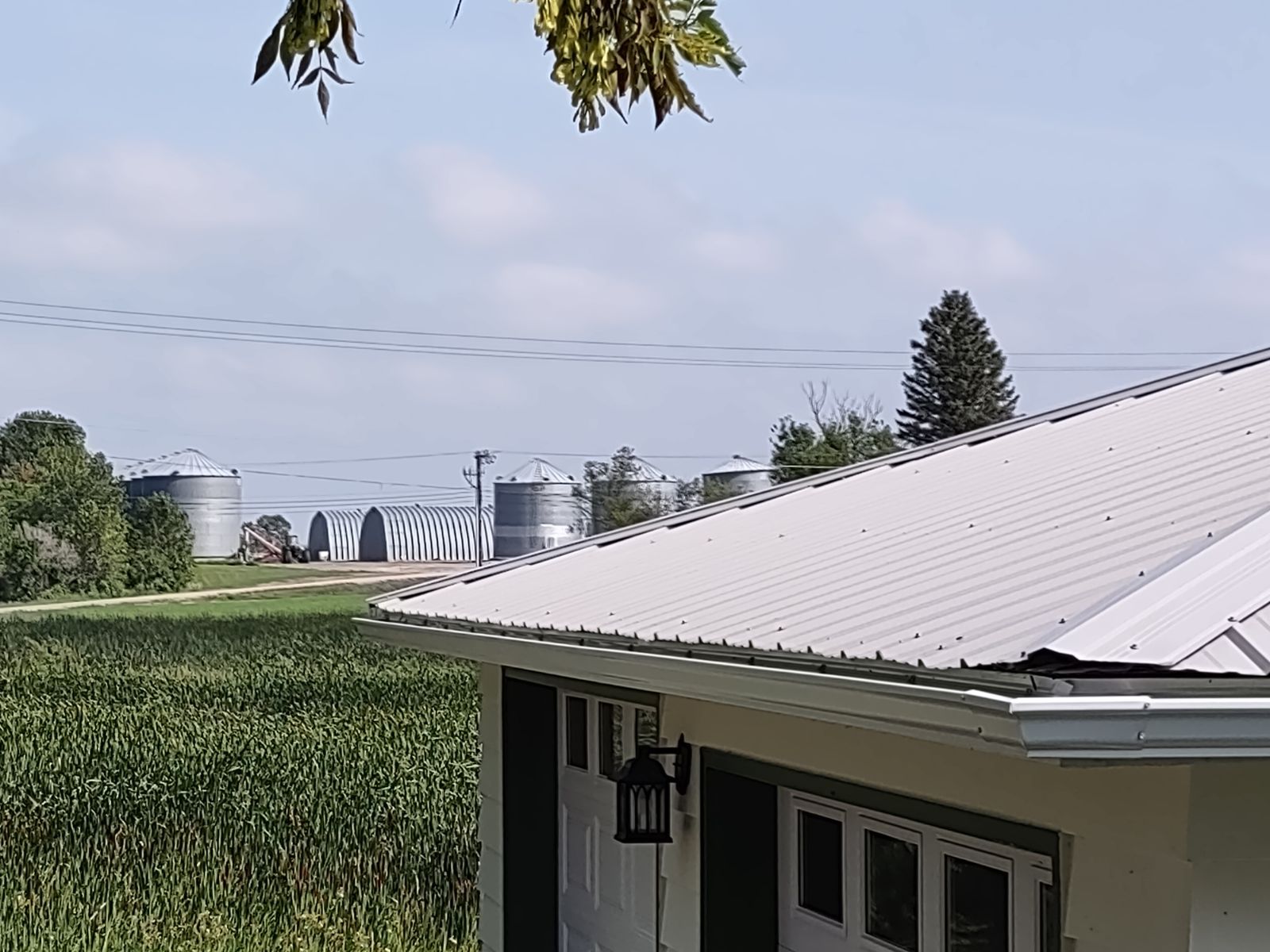 Rural landscape with green fields, farm buildings, and a white-roofed house in the foreground.