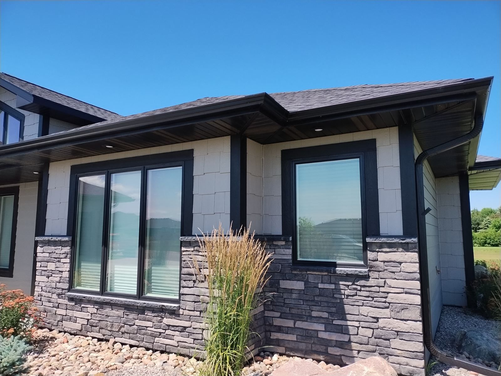 Exterior of a modern stone house with large black-framed windows and a tiled roof