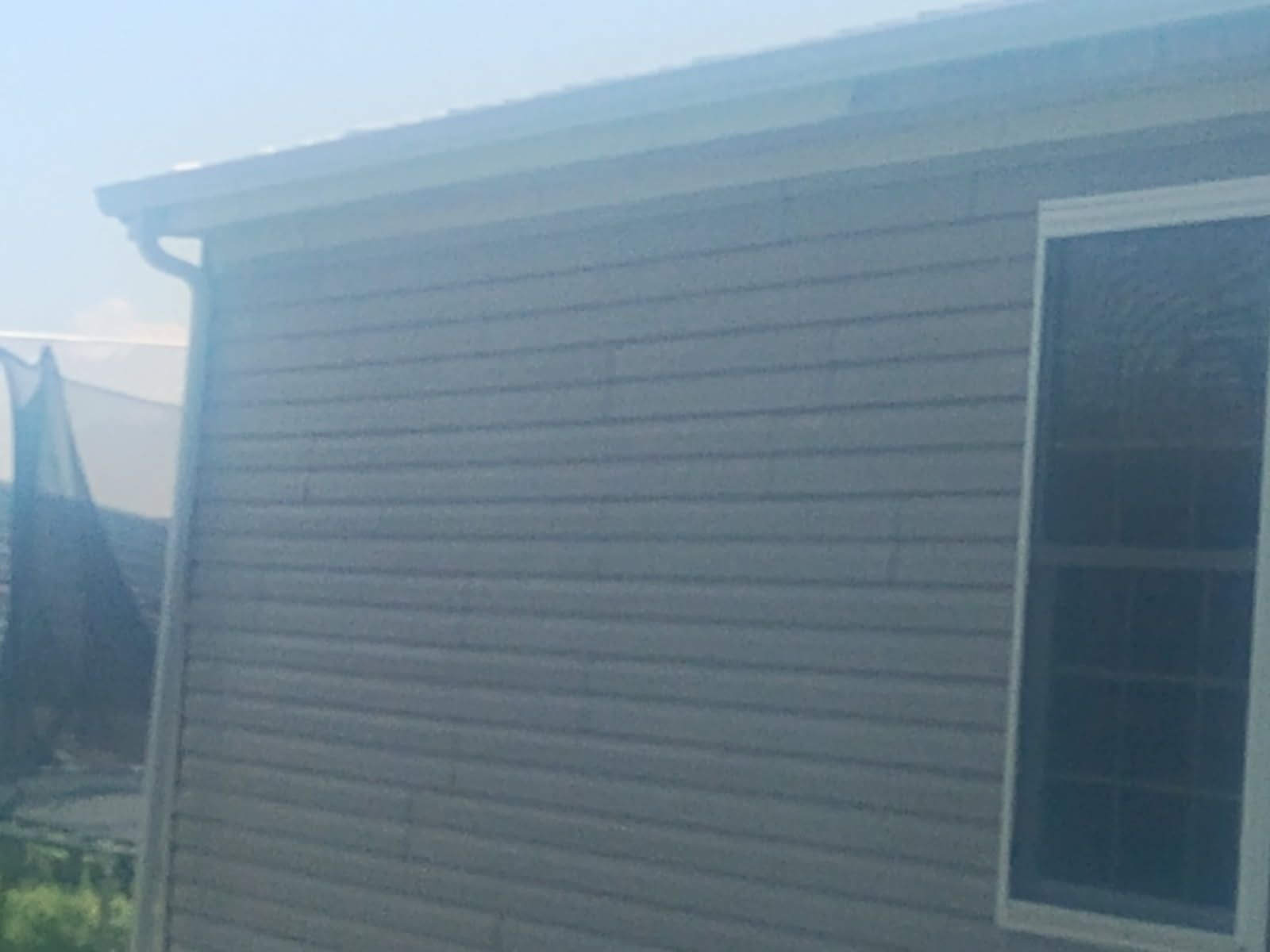 Exterior wall of a beige house with a window, viewed in bright sunlight