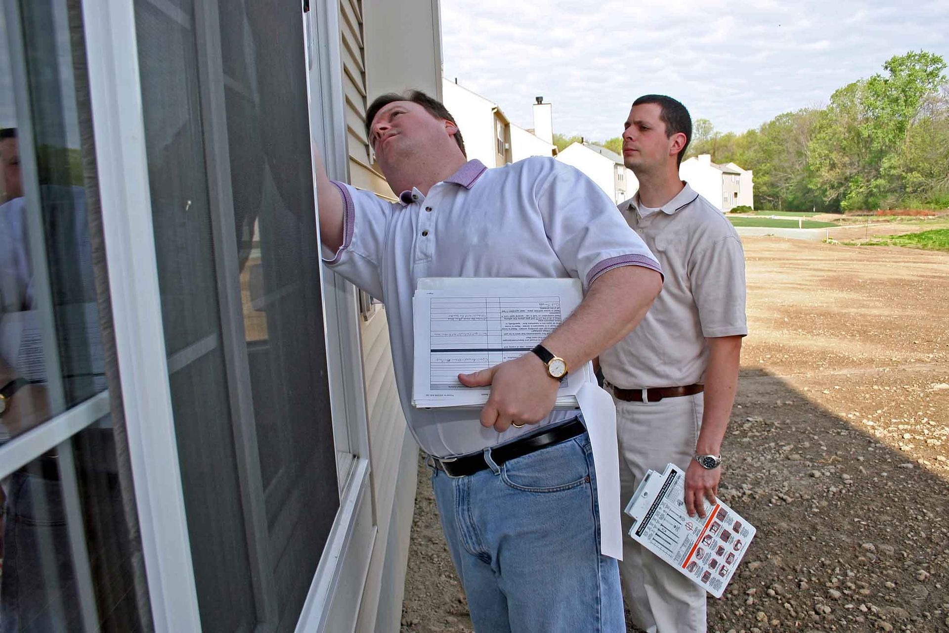 Two men are looking at a window and one is holding a calculator