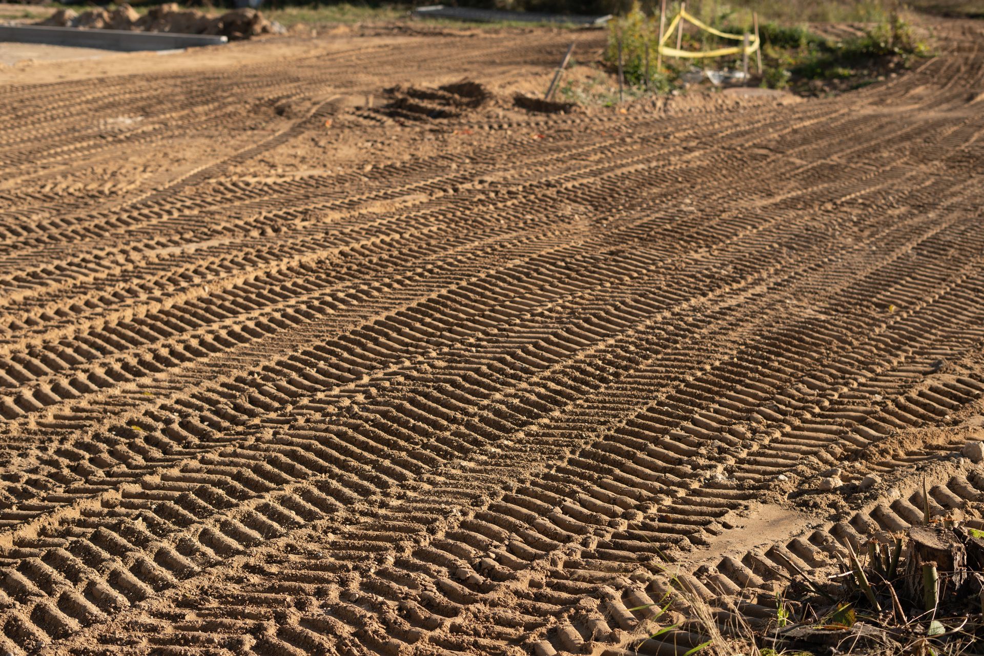 Tire tracks in freshly graded dirt, diagonal lines across the field, construction site.
