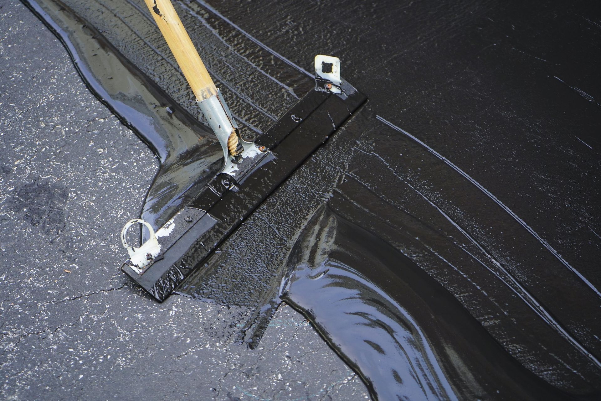 A person is applying black sealant to asphalt with a squeegee.