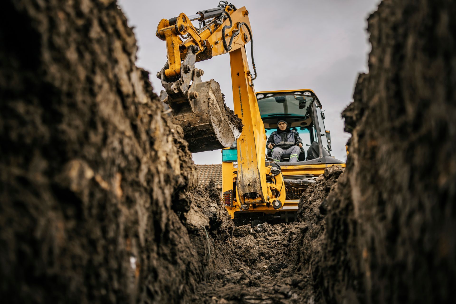 An excavator digging a trench, operator in the cab, working in a muddy area.