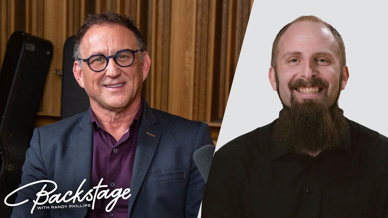 A man with glasses and a beard is sitting next to another man with a beard.