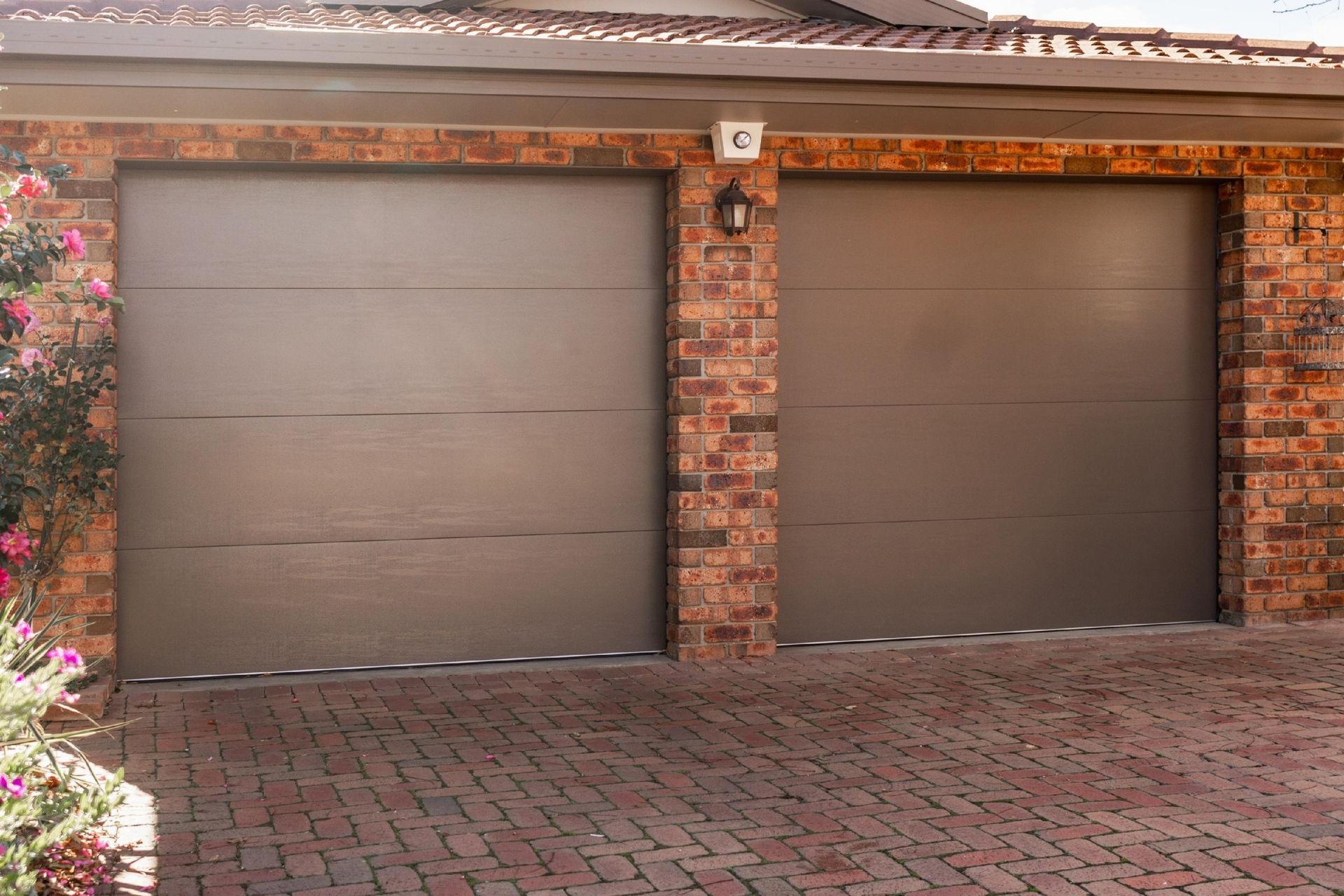 Two brown garage doors on a brick house with a paved driveway.