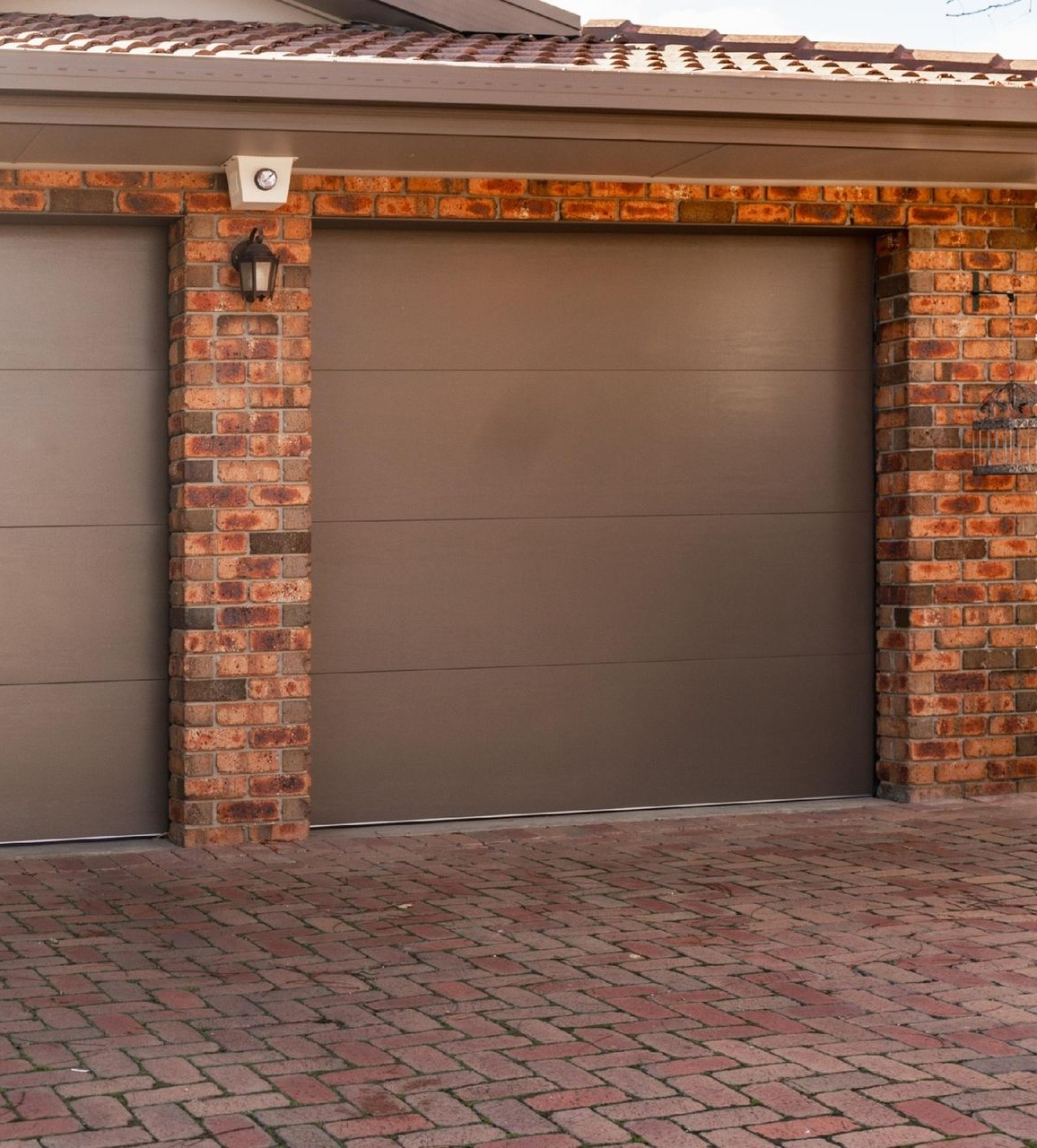 Two gray garage doors with brick columns in a residential setting.