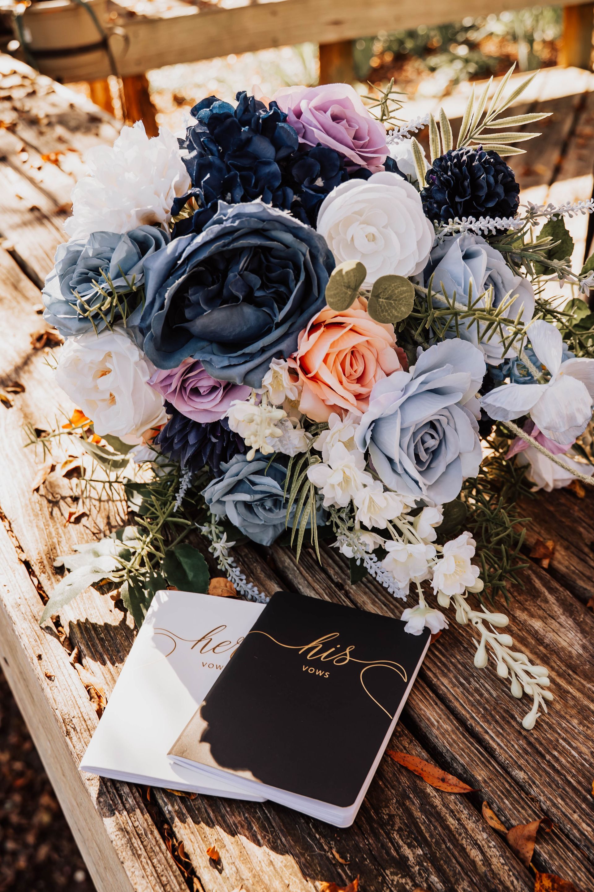 Bouquet of blue, white, and peach flowers beside a black-and-white booklet on a rustic wooden surface