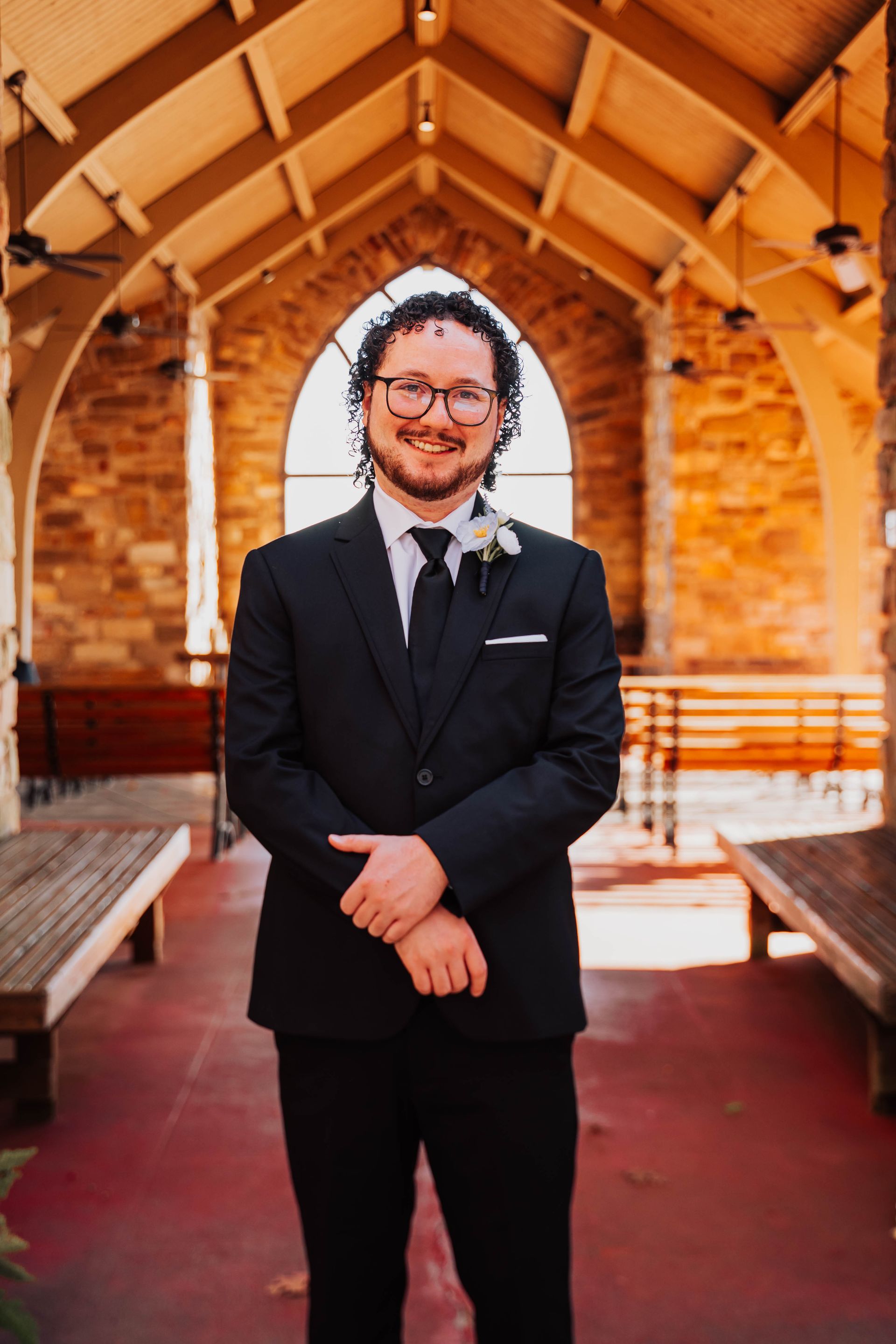 Man in a black suit standing in a church aisle, smiling under a wooden archway