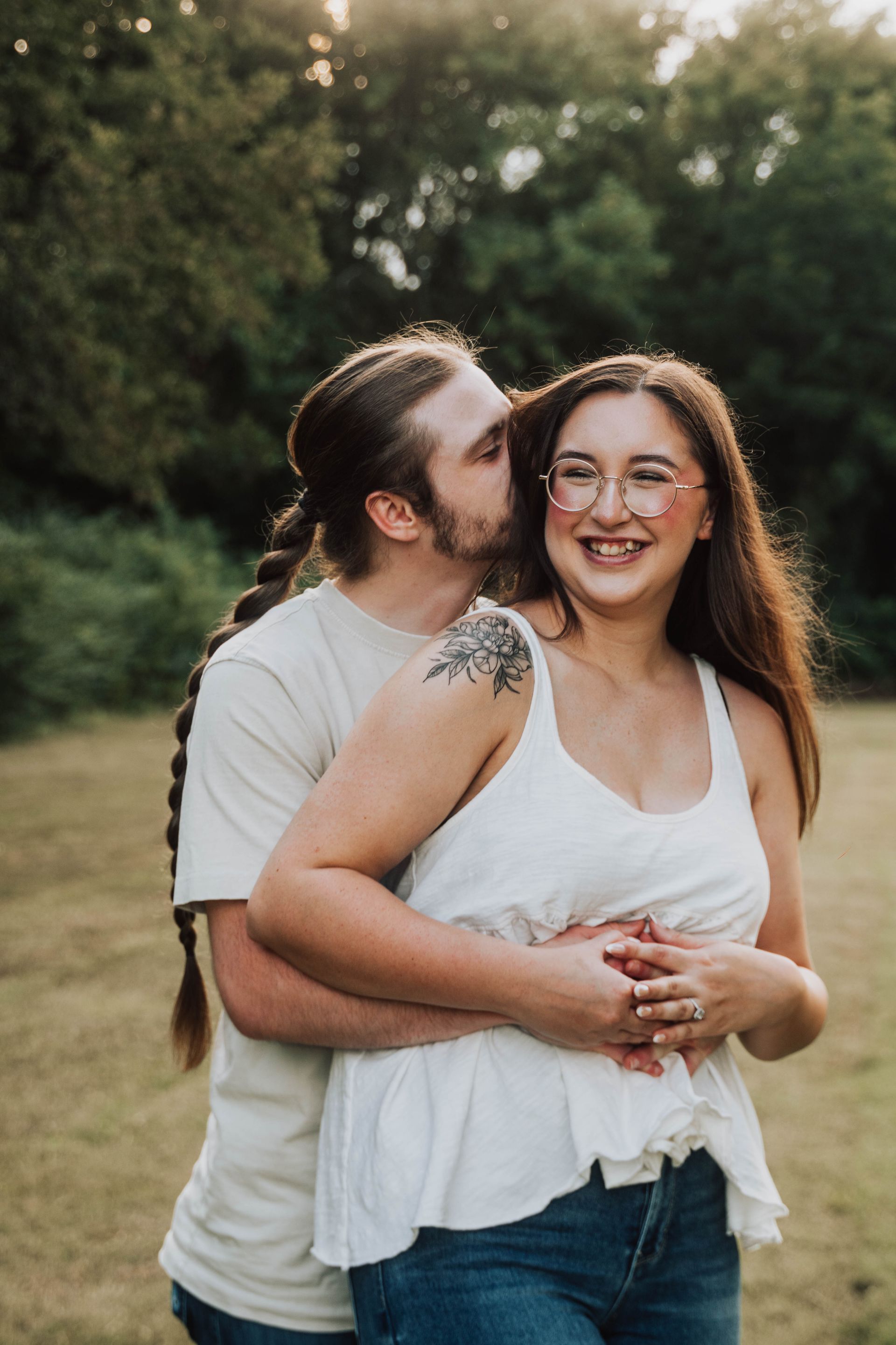 Couple embracing outdoors, smiling in a grassy field at sunset