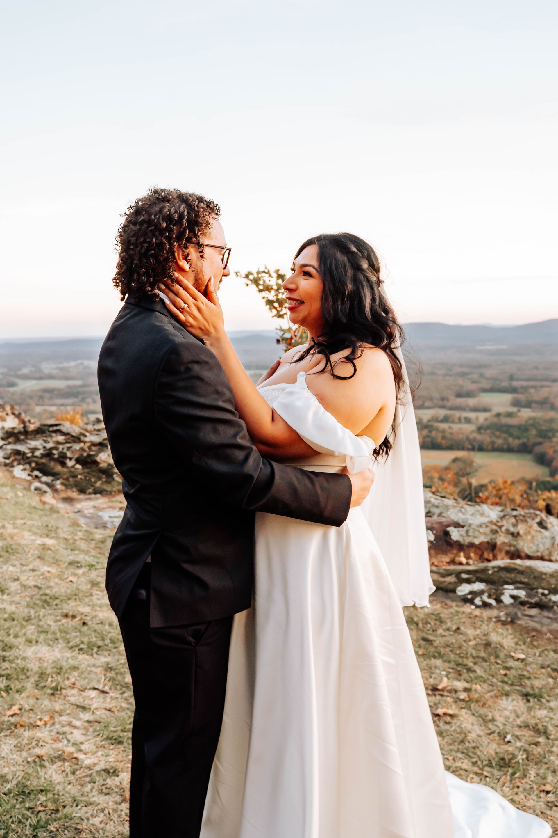 Couple embracing outdoors at sunset, with rolling hills in the background.