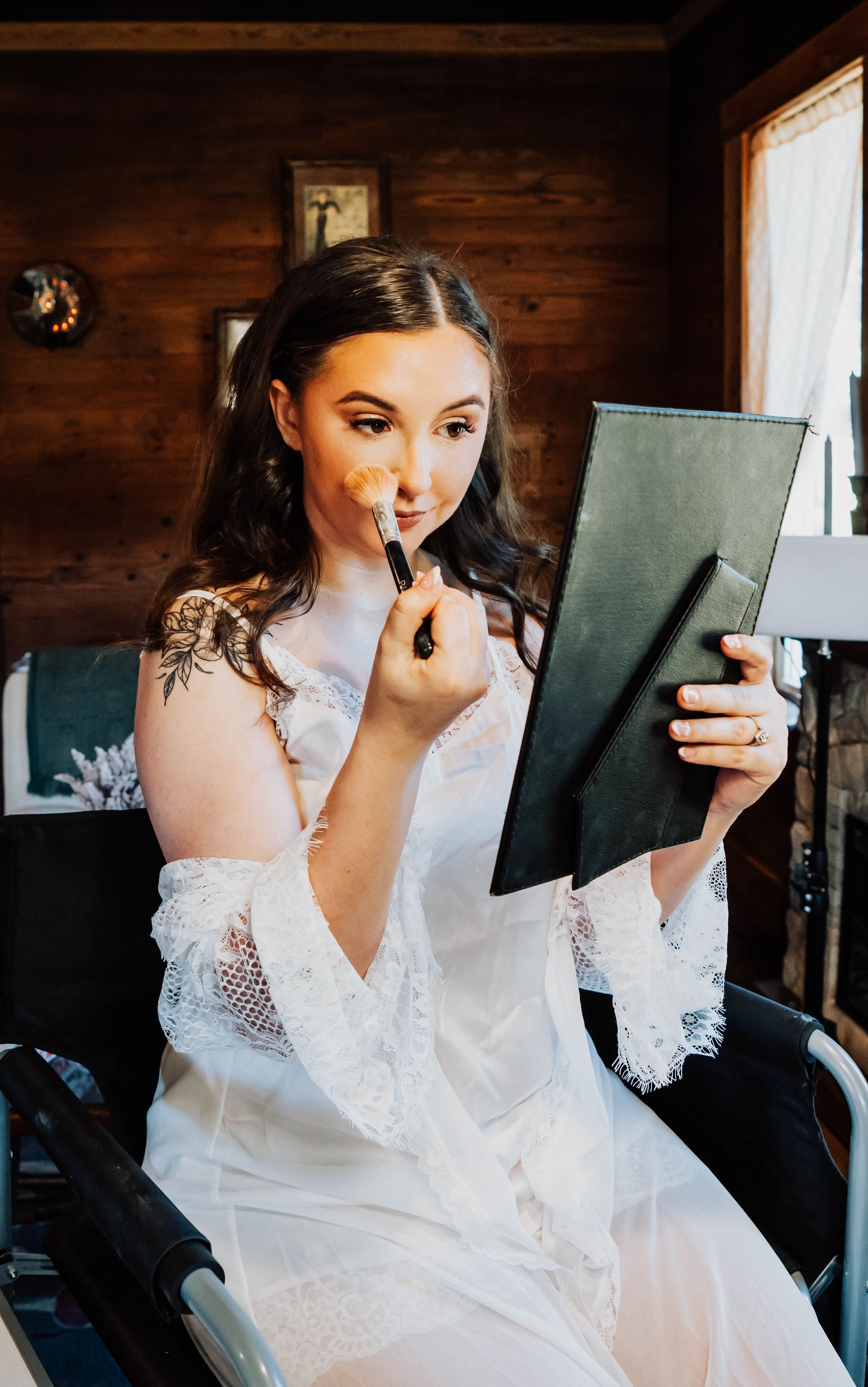 Woman in a white robe applying lipstick while looking into a mirror in a wood-paneled room.