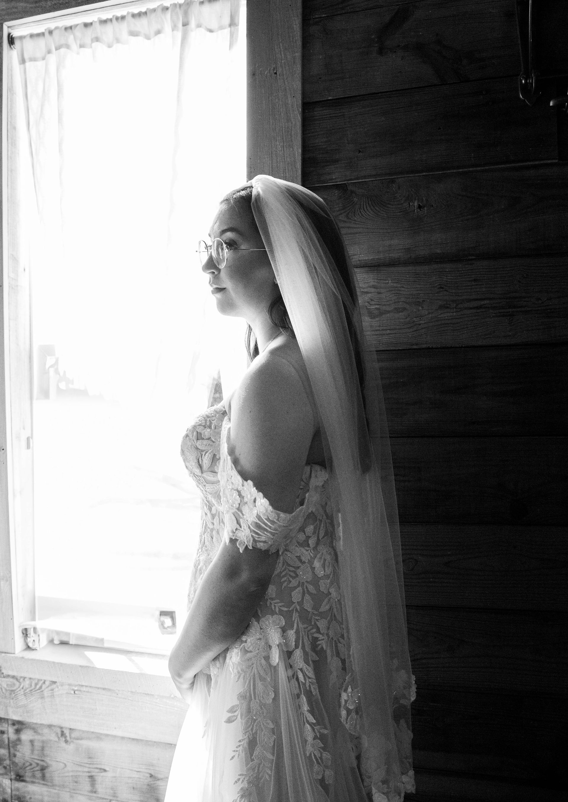 Bride in a veil standing by a bright window in a rustic room