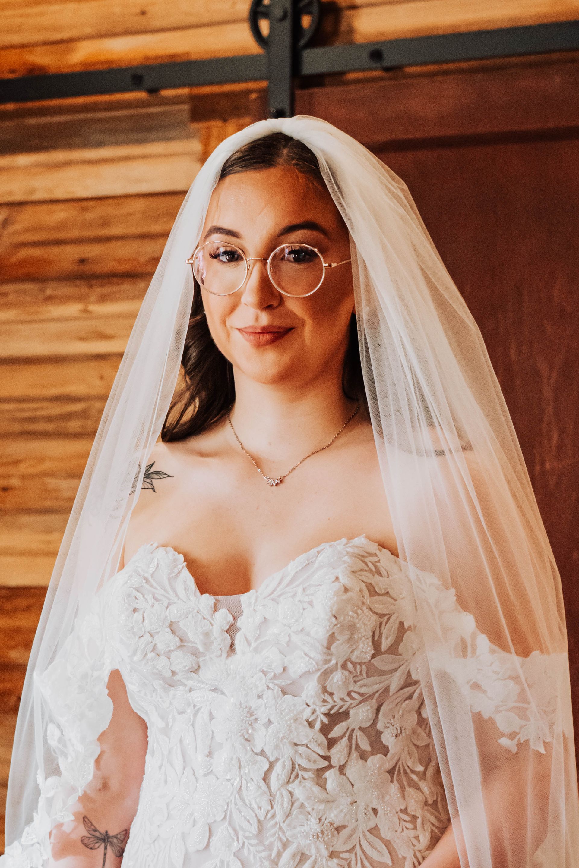 Bride in a white lace dress and veil, smiling indoors with warm wooden background.