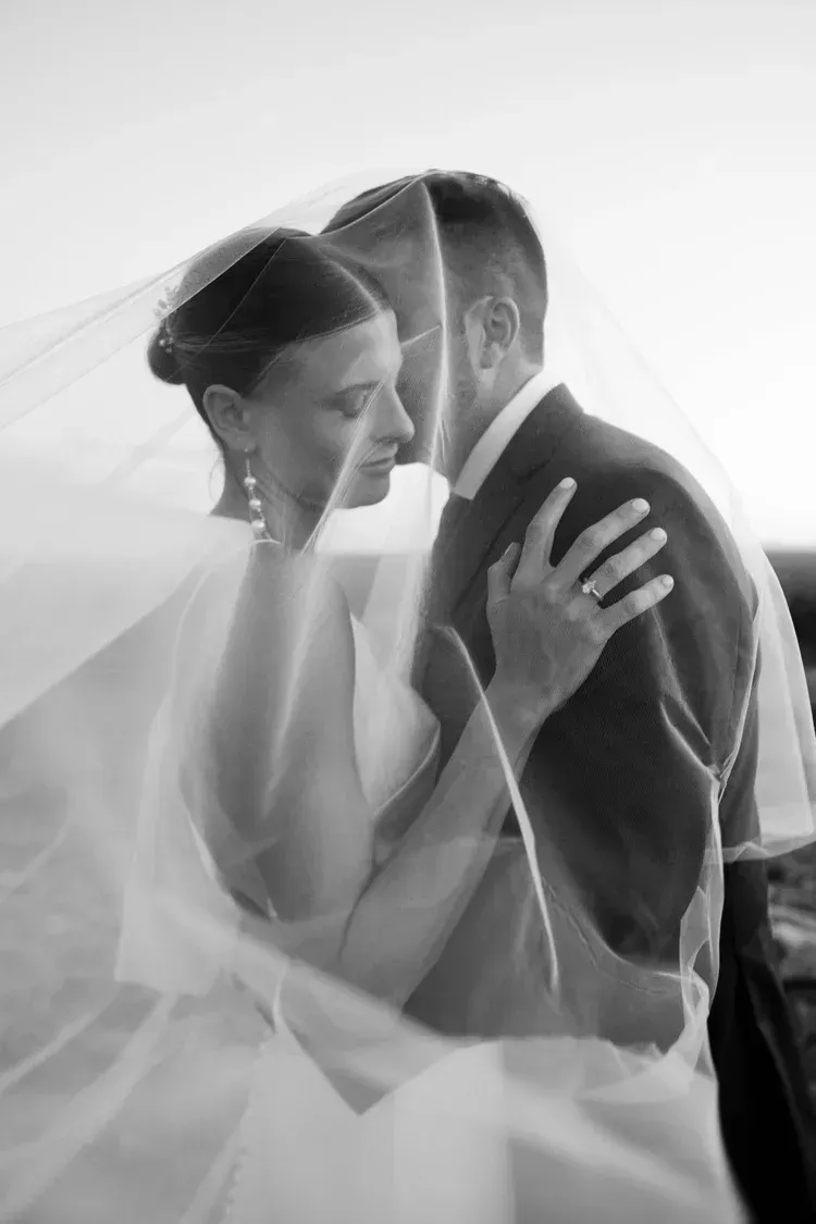 Bride and groom kissing under a translucent veil in black and white