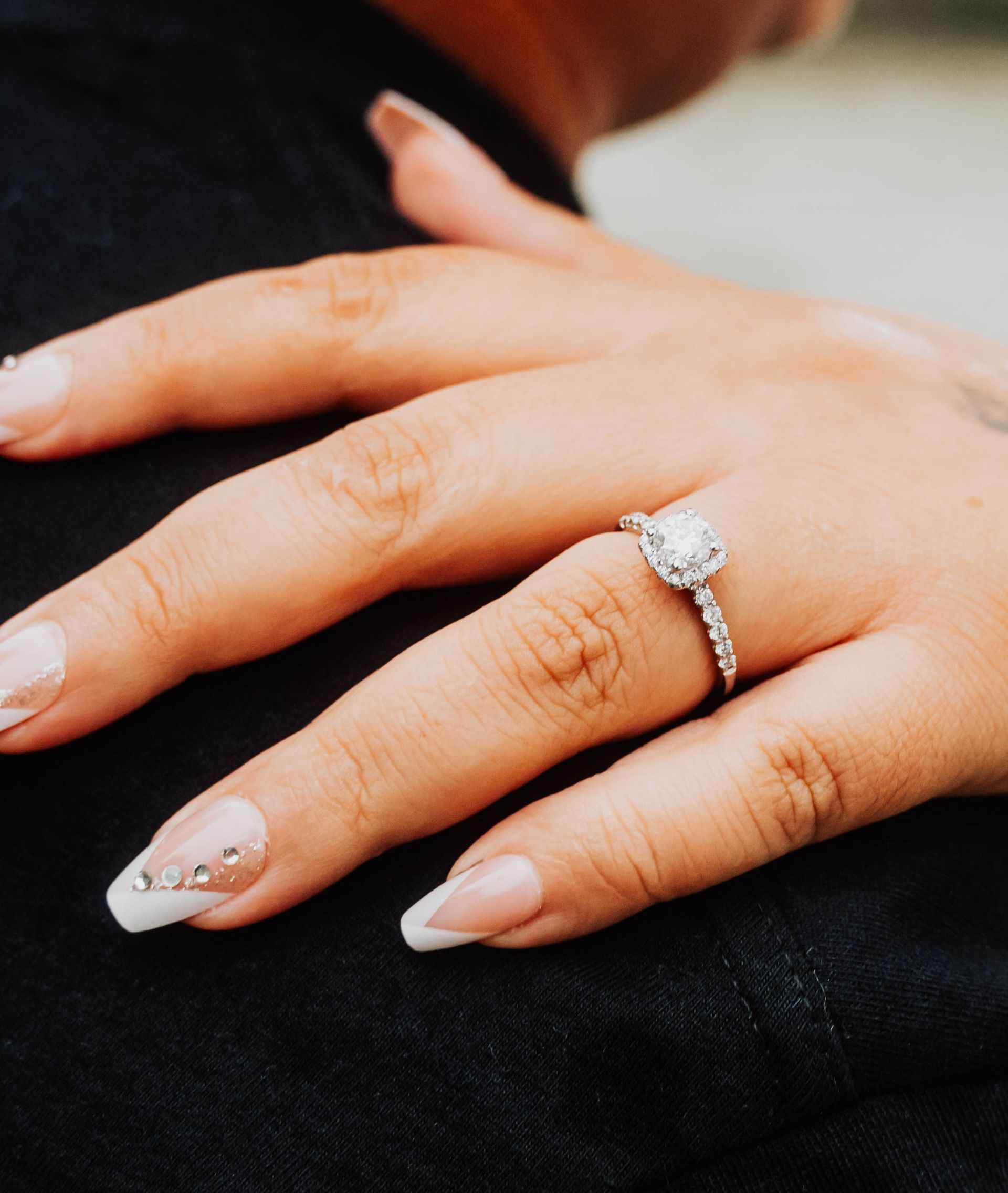 Hand with a diamond engagement ring resting on a dark fabric background