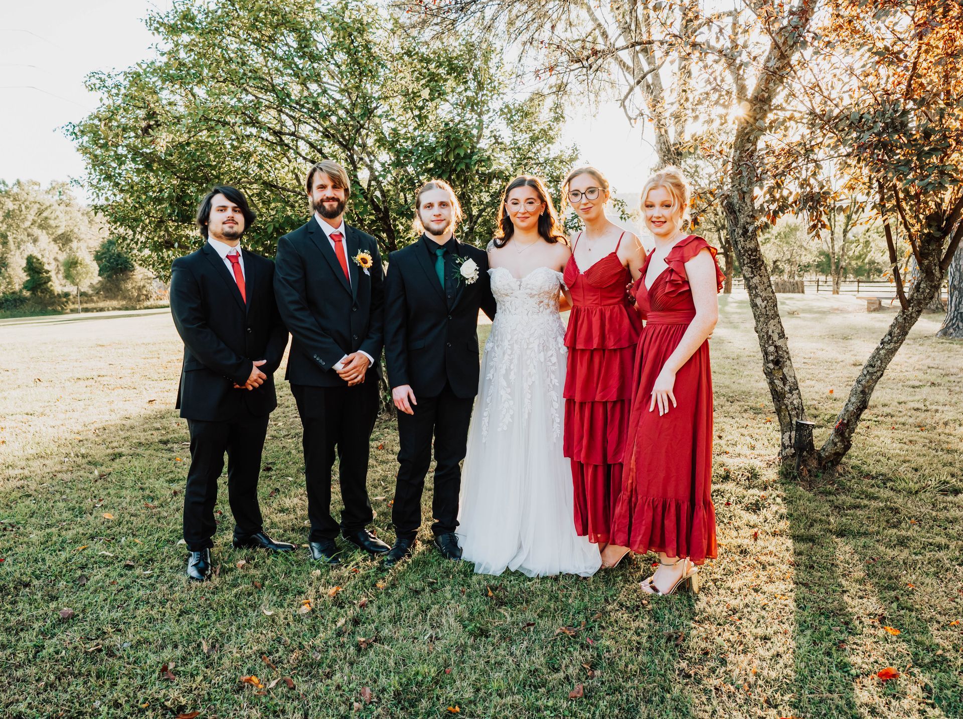 Six people in formal attire standing outdoors by trees, posing for a group photo.