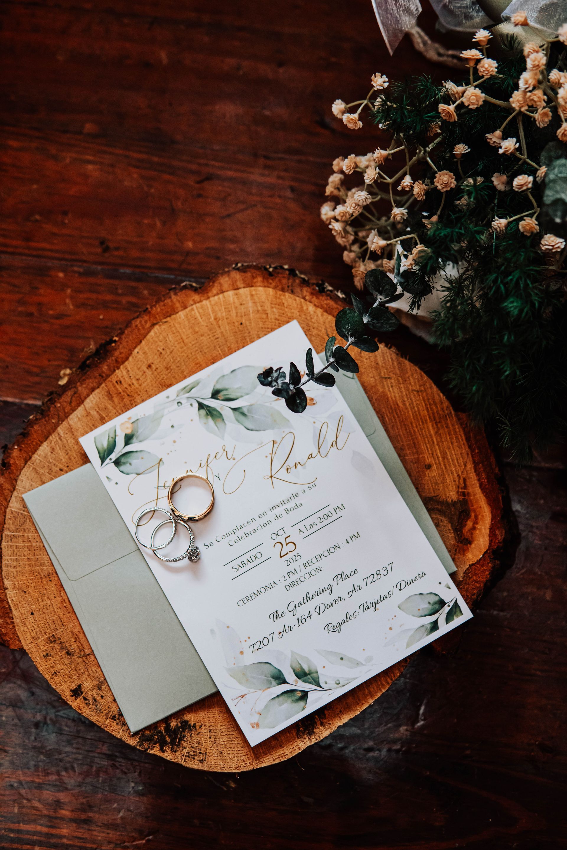 Wedding invitation on a wooden table with rings and greenery, styled in soft neutral tones