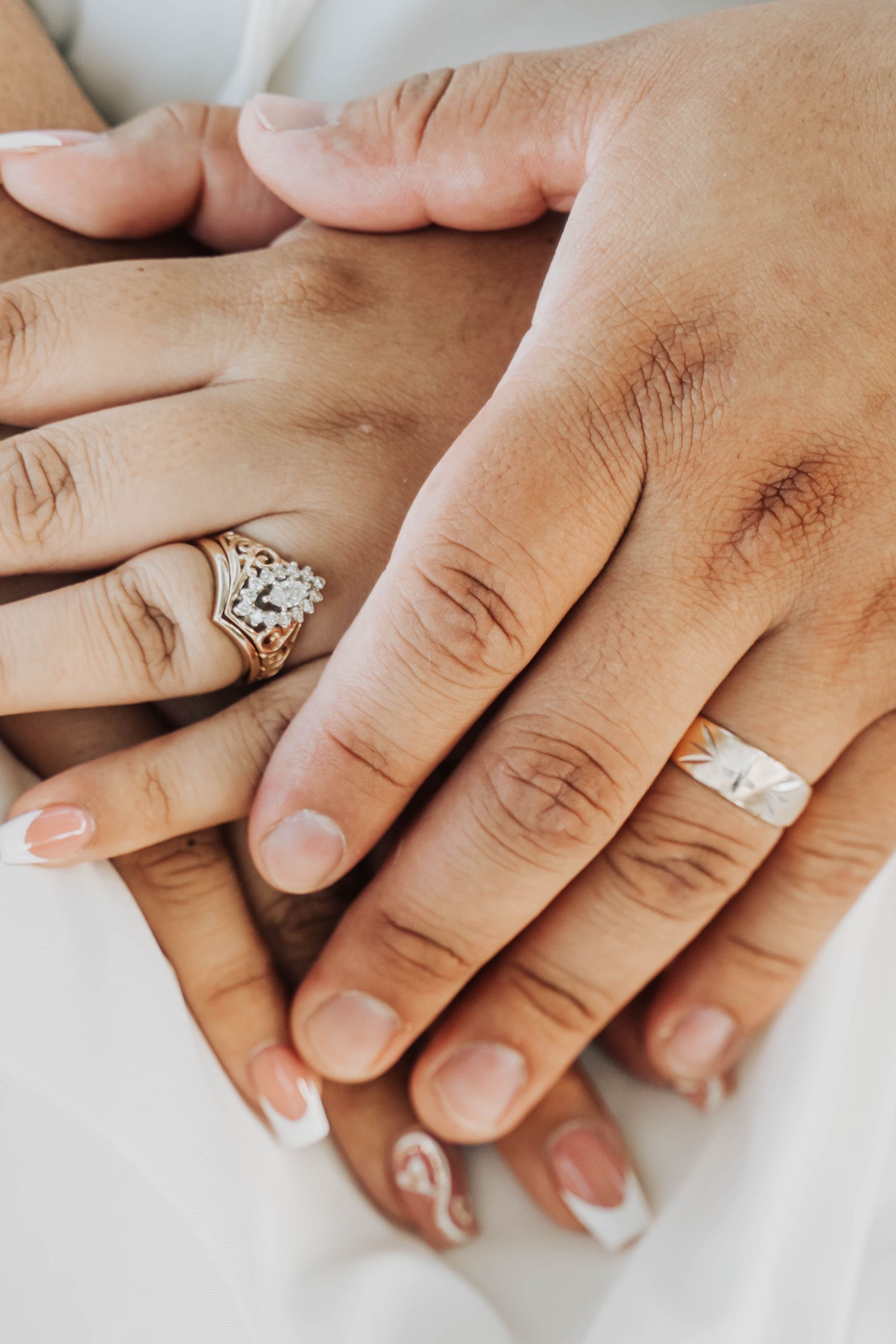 Hands stacked together with wedding rings, including a diamond ring and gold bands.