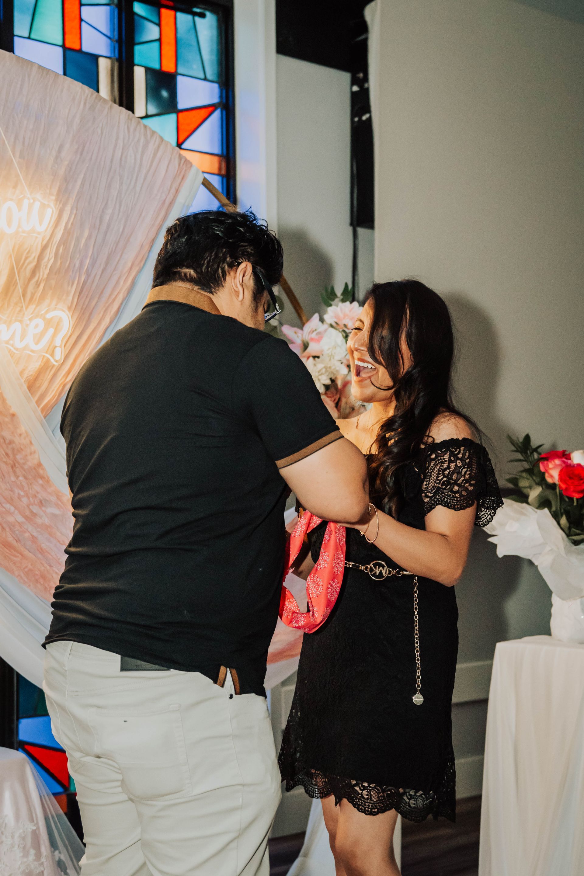 Two people chatting at an indoor celebration, with a black dress and red gift bag visible.