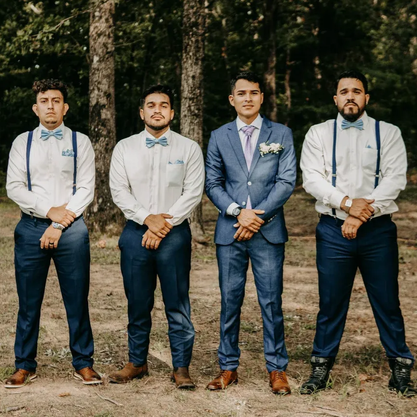 Four men in dress shirts, ties, and suits standing outdoors in a wooded area.