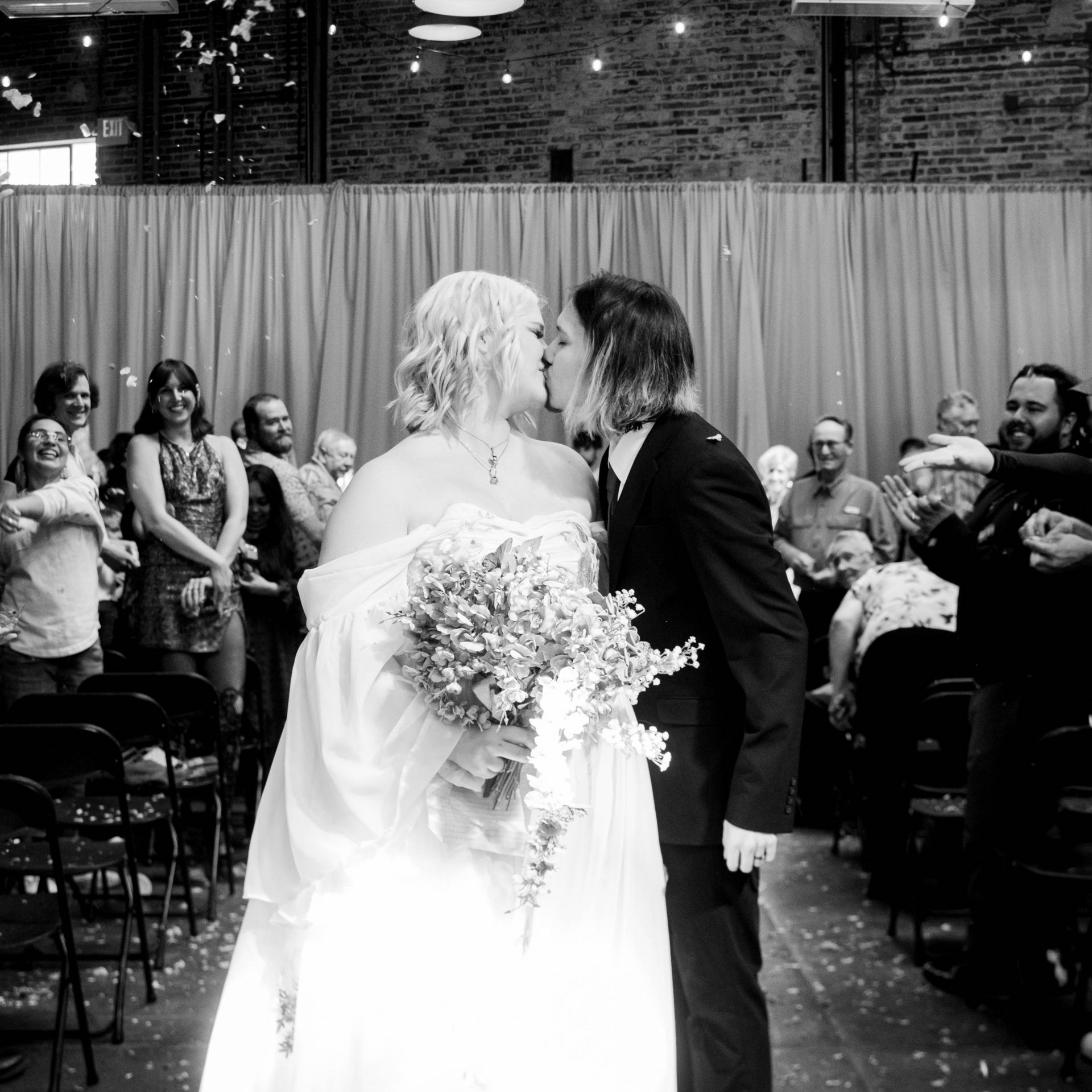 Bride and groom kiss at wedding ceremony aisle with guests seated on both sides