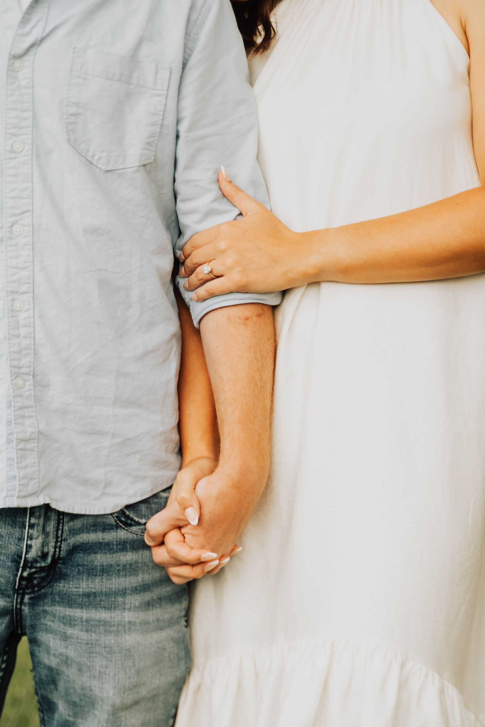 Two people holding hands, one in a light blue shirt and jeans, the other in a white dress.