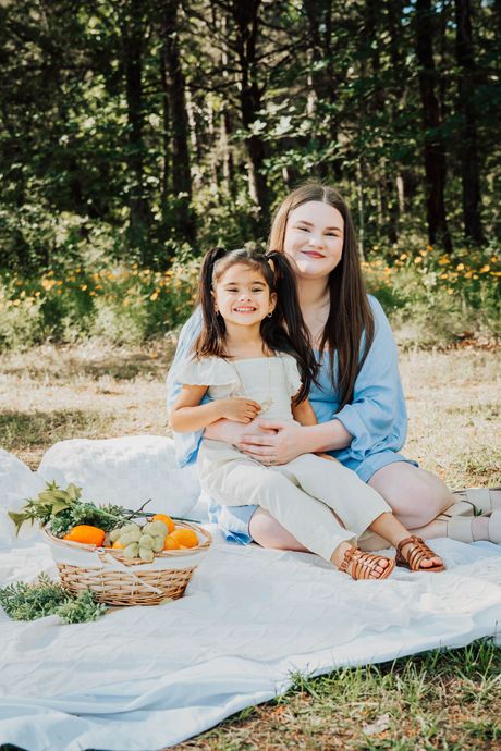 Two people sitting on a picnic blanket outdoors with fruit and bread in a sunny wooded area