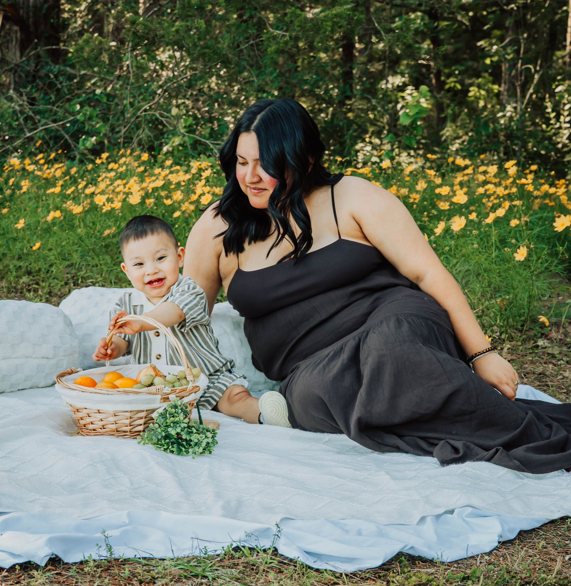 Two people sitting on a white blanket in a flowered outdoor setting, sharing a picnic basket.