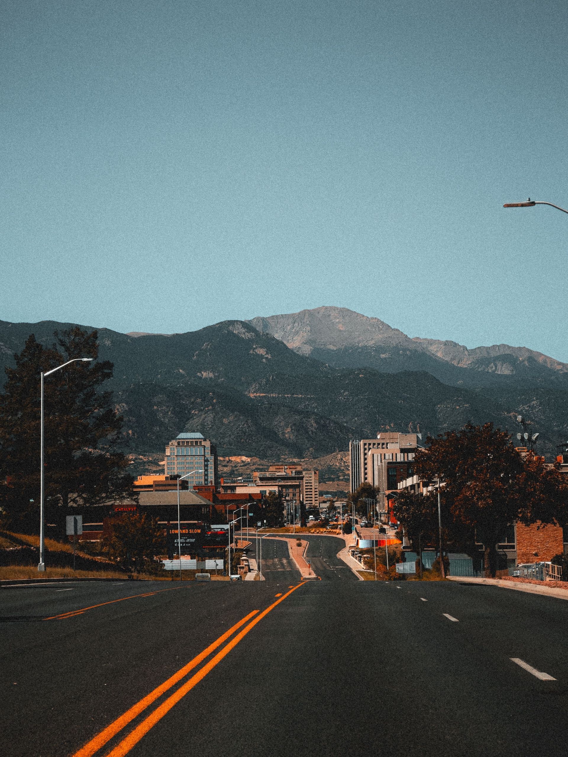 Road leading toward a mountain town under a clear blue sky at dusk