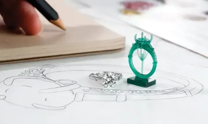 Hand sketch of a green ring design beside a pencil and notebook on a desk