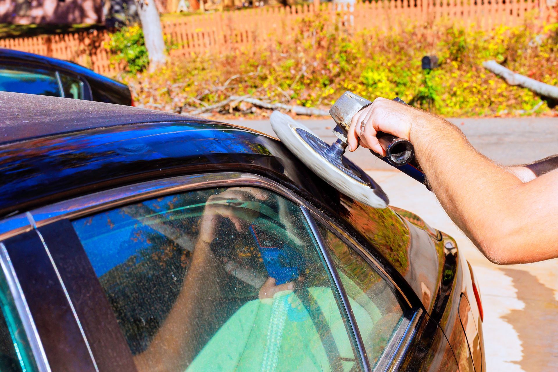 Person polishing a black car windshield with a cloth outdoors in bright sunlight
