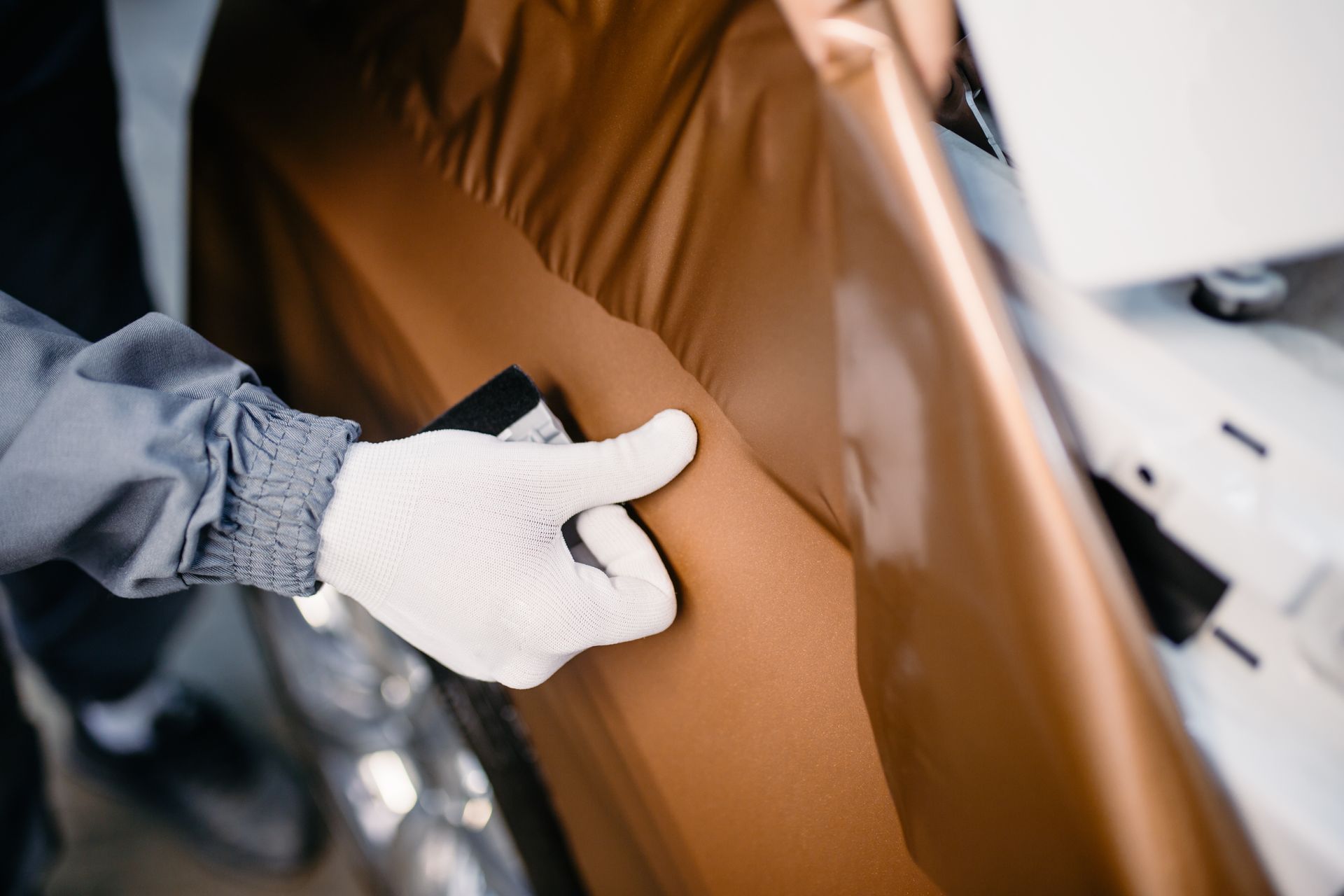 Gloved hand peeling protective film from a tan car seat upholstery