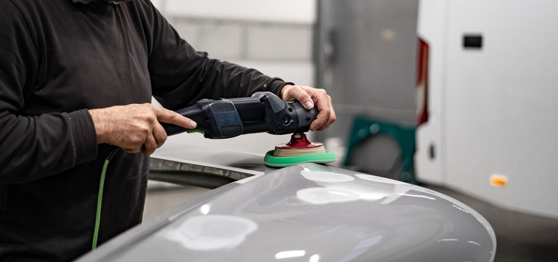 Person polishing a gray car hood with a buffer in an auto shop