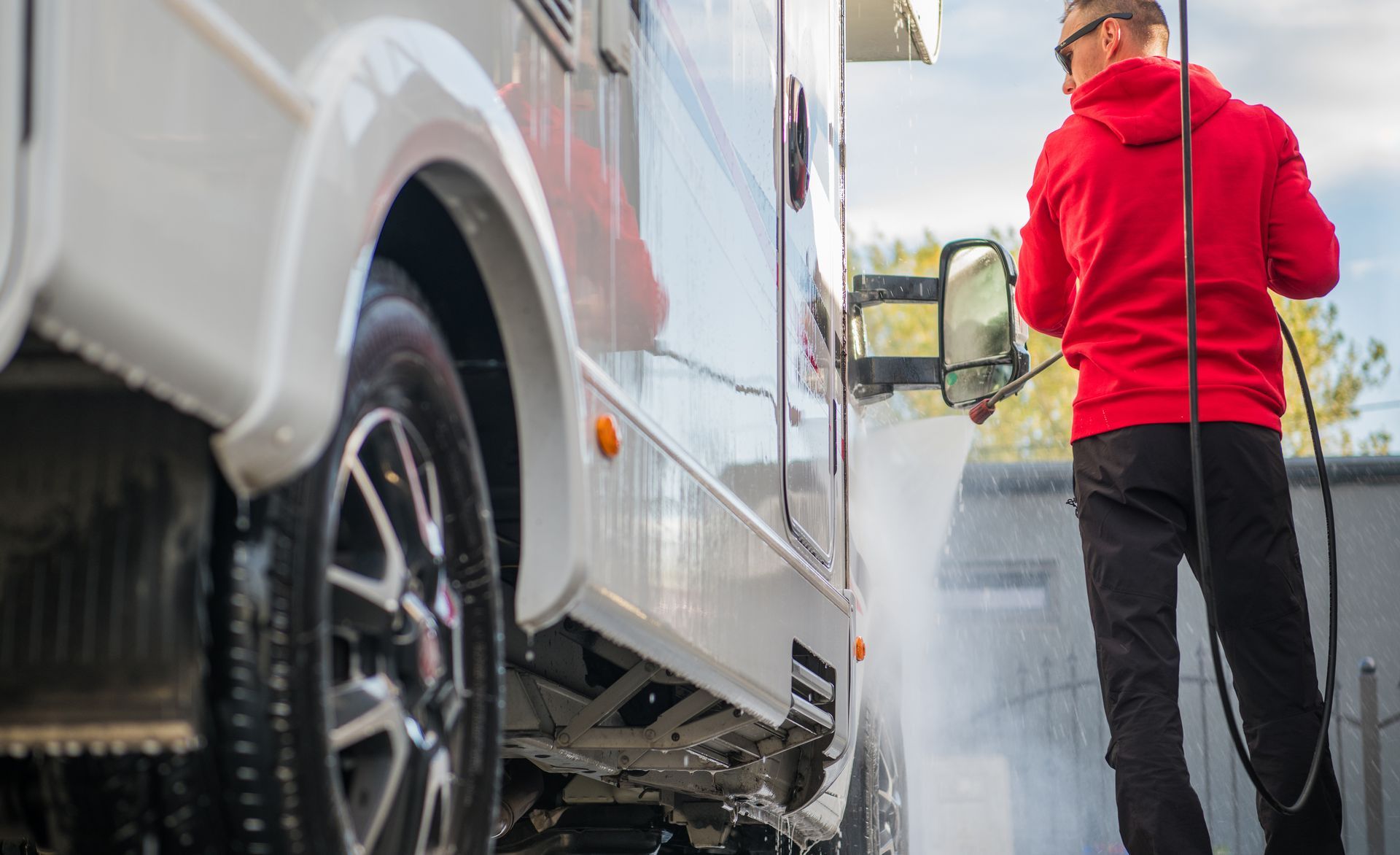 Person in a red jacket cleaning a white truck with a pressure washer outdoors