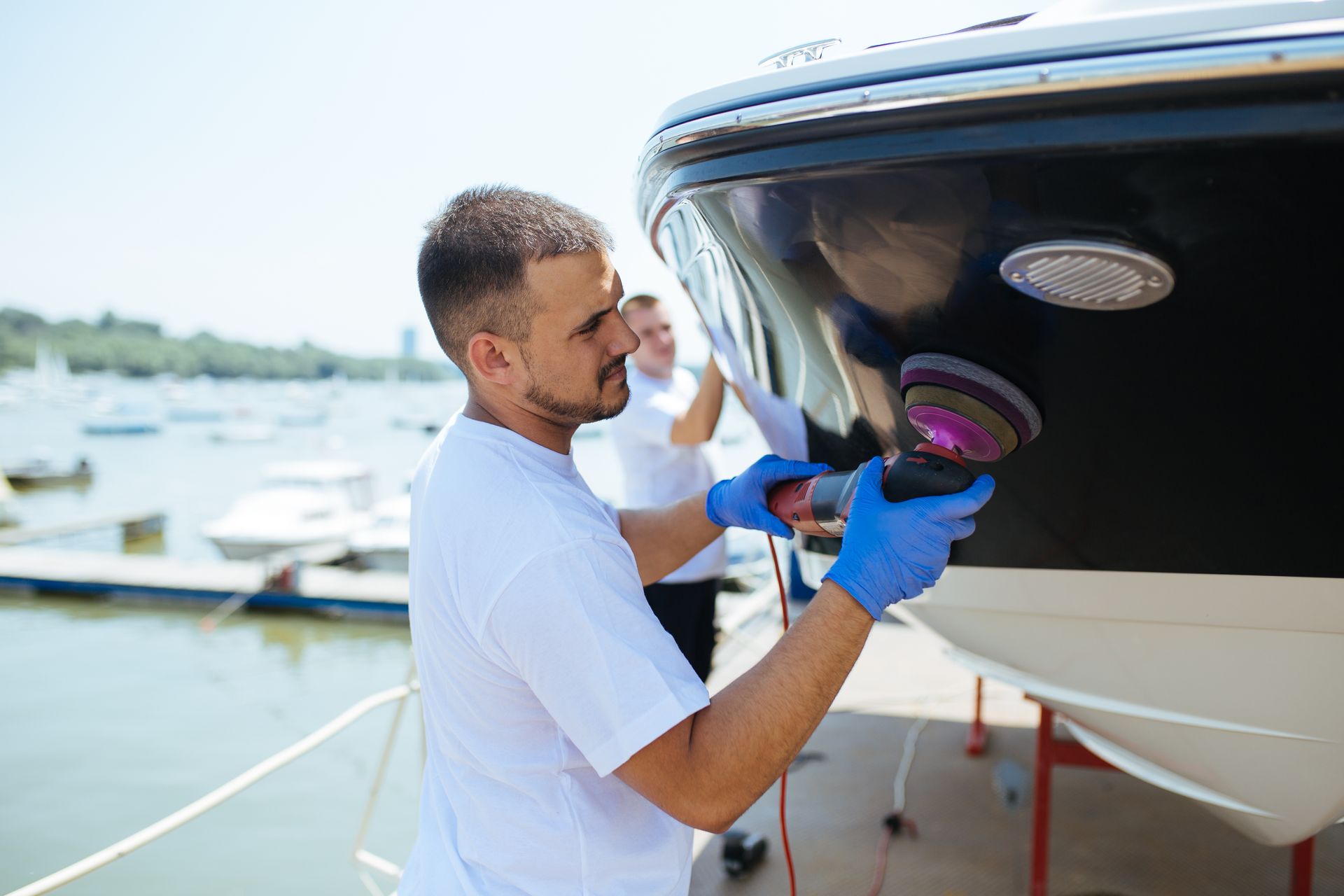 Man polishing a white boat hull with a buffer at a marina