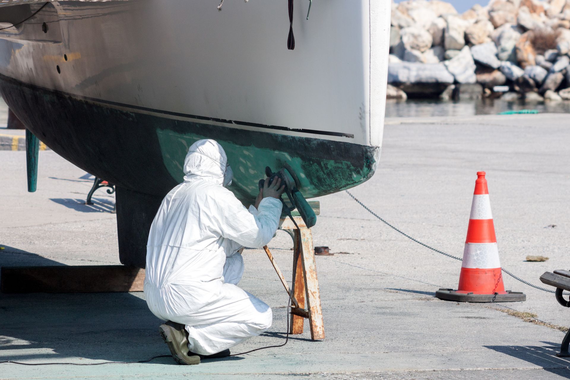 Person in white protective suit working on a boat hull near a cone at a dock