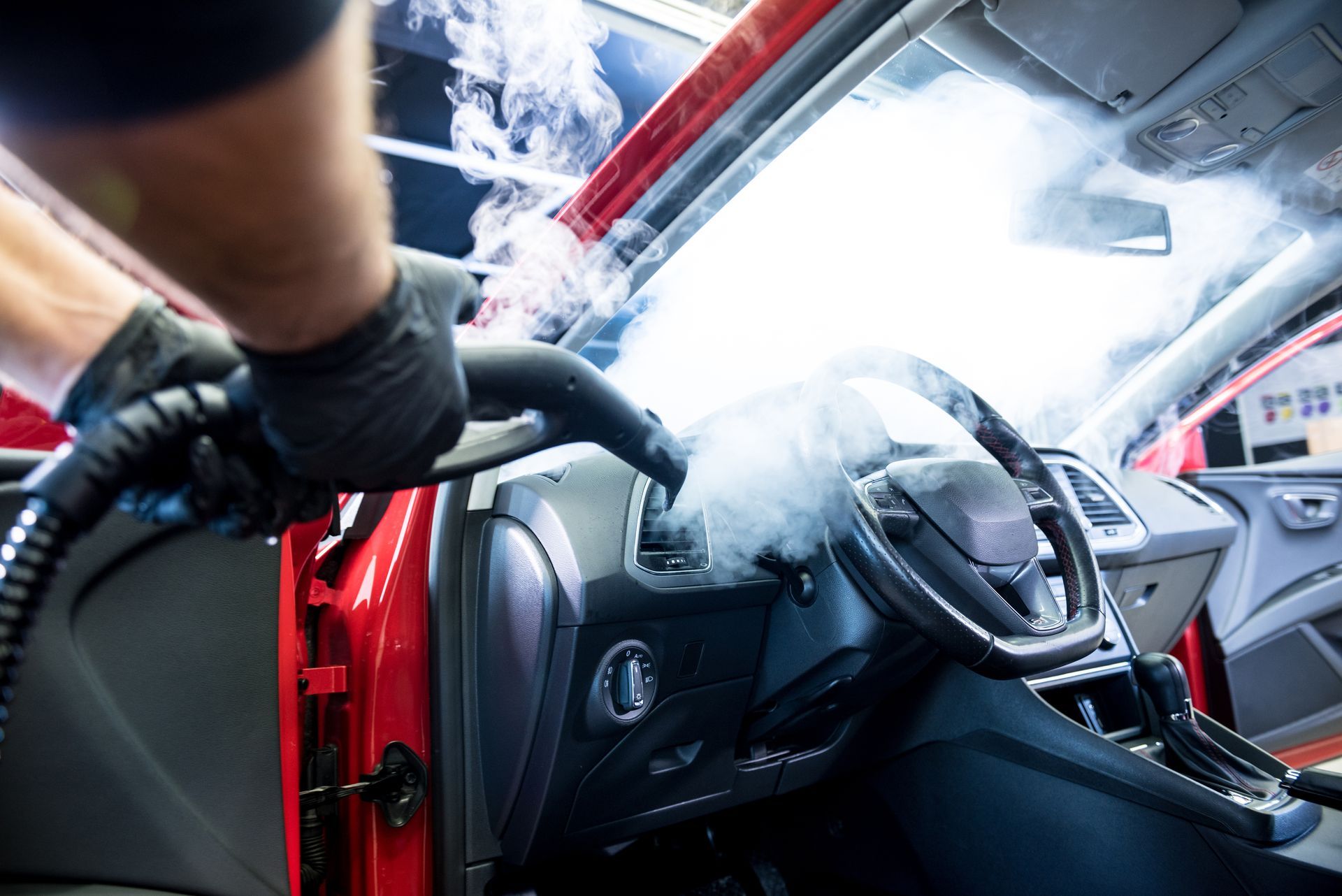 Mechanic using a vacuum on a red car interior with the driver’s door open