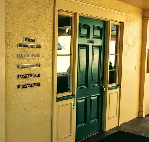 Green door with side windows and a wall-mounted directory in a beige building hallway