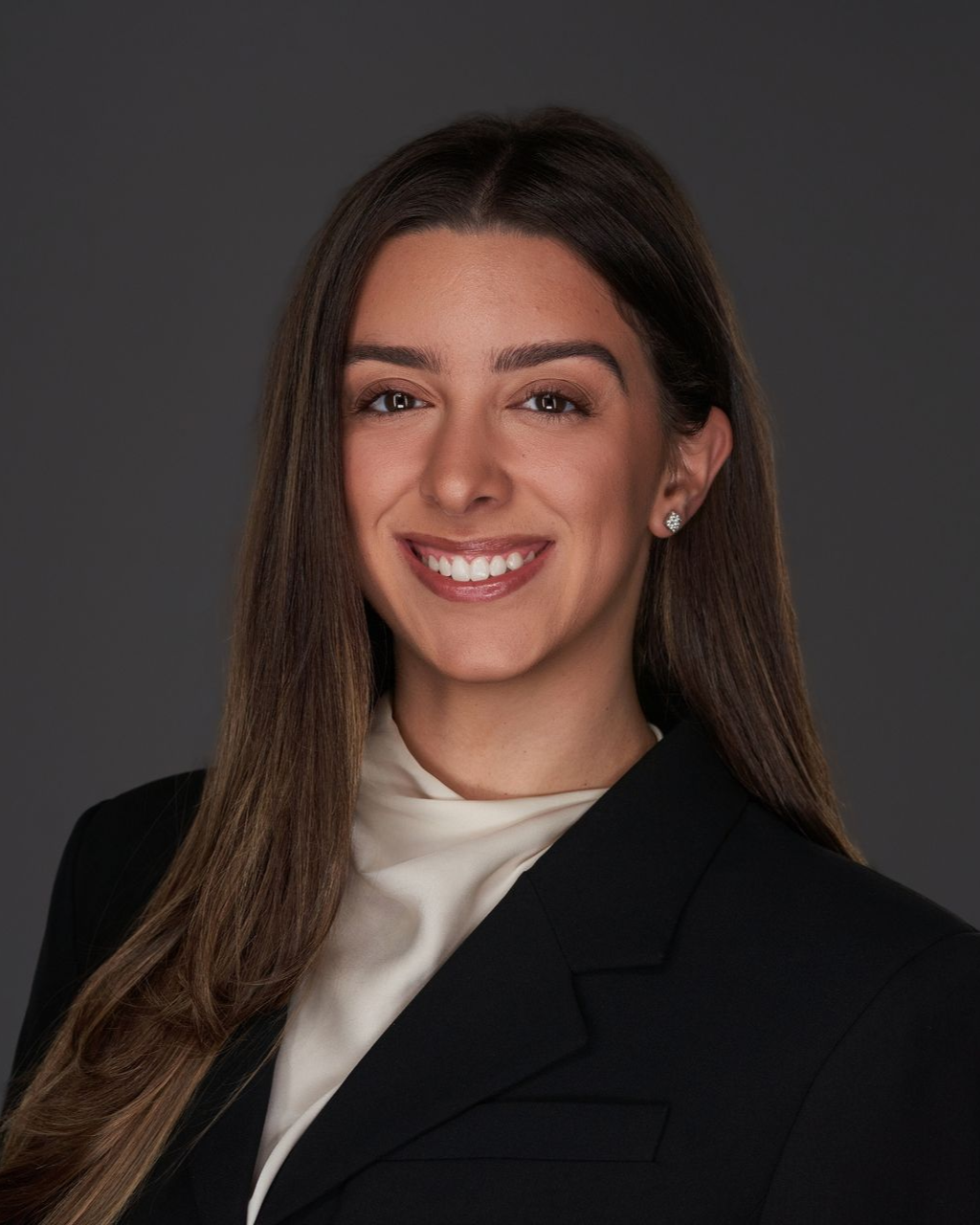 Carolina Blanco. A woman with dark hair, smiling and wearing a dark blazer.