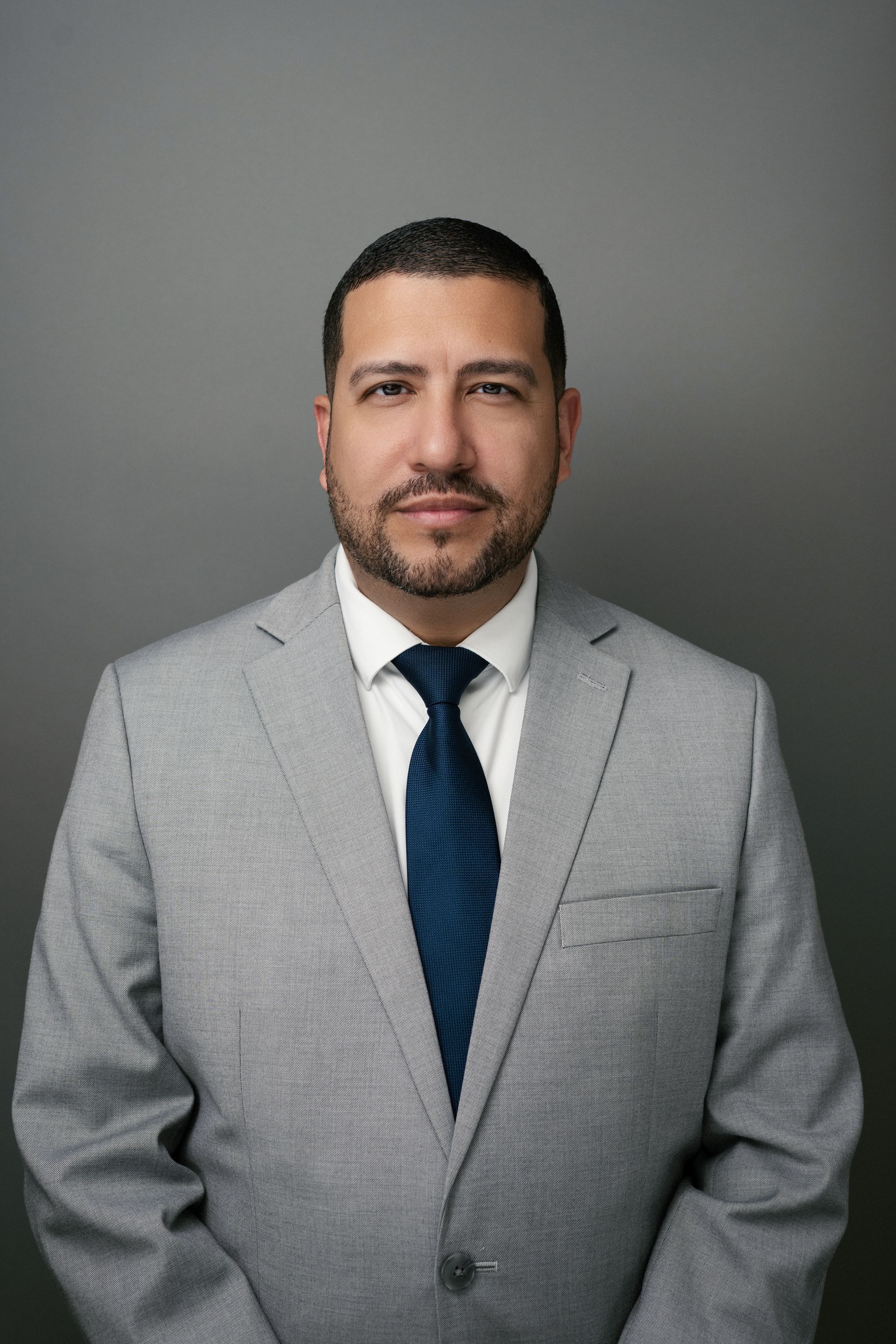Miguel Planas. A man with dark hair and a soft smile, wearing a gray suit and navy tie.