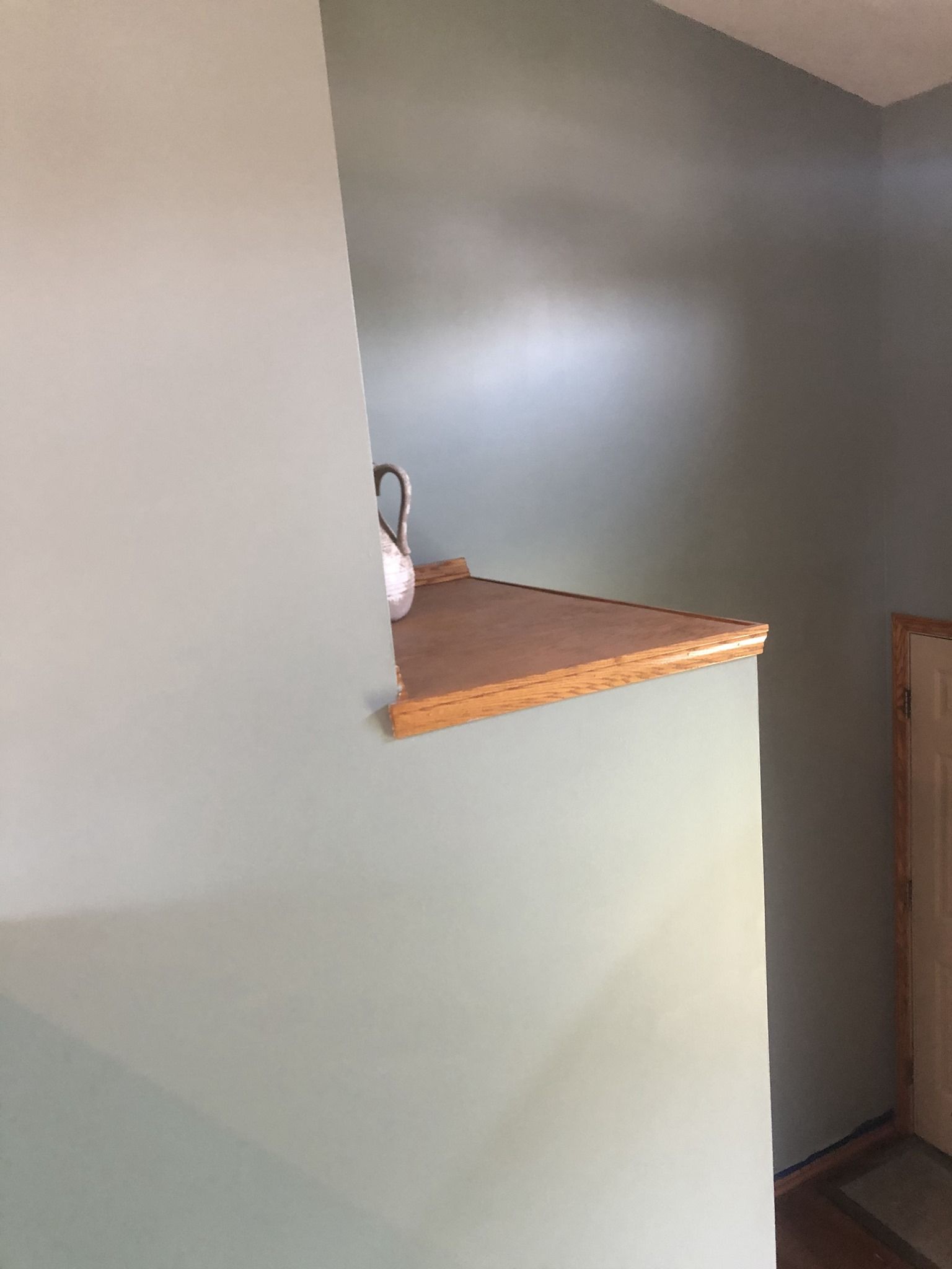 A corner of a room with a wooden shelf on the wall.