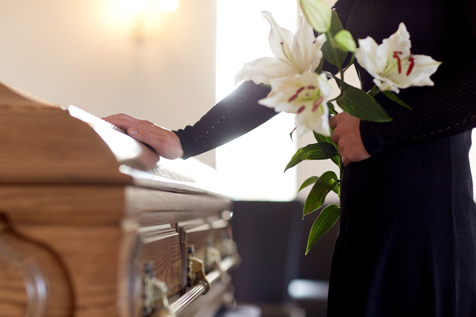 Person beside a wooden casket placing white lilies during a funeral service