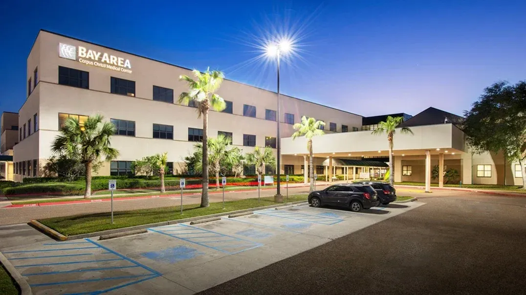 Nighttime exterior of a hotel with lit parking lot, palm trees, and a car in front.