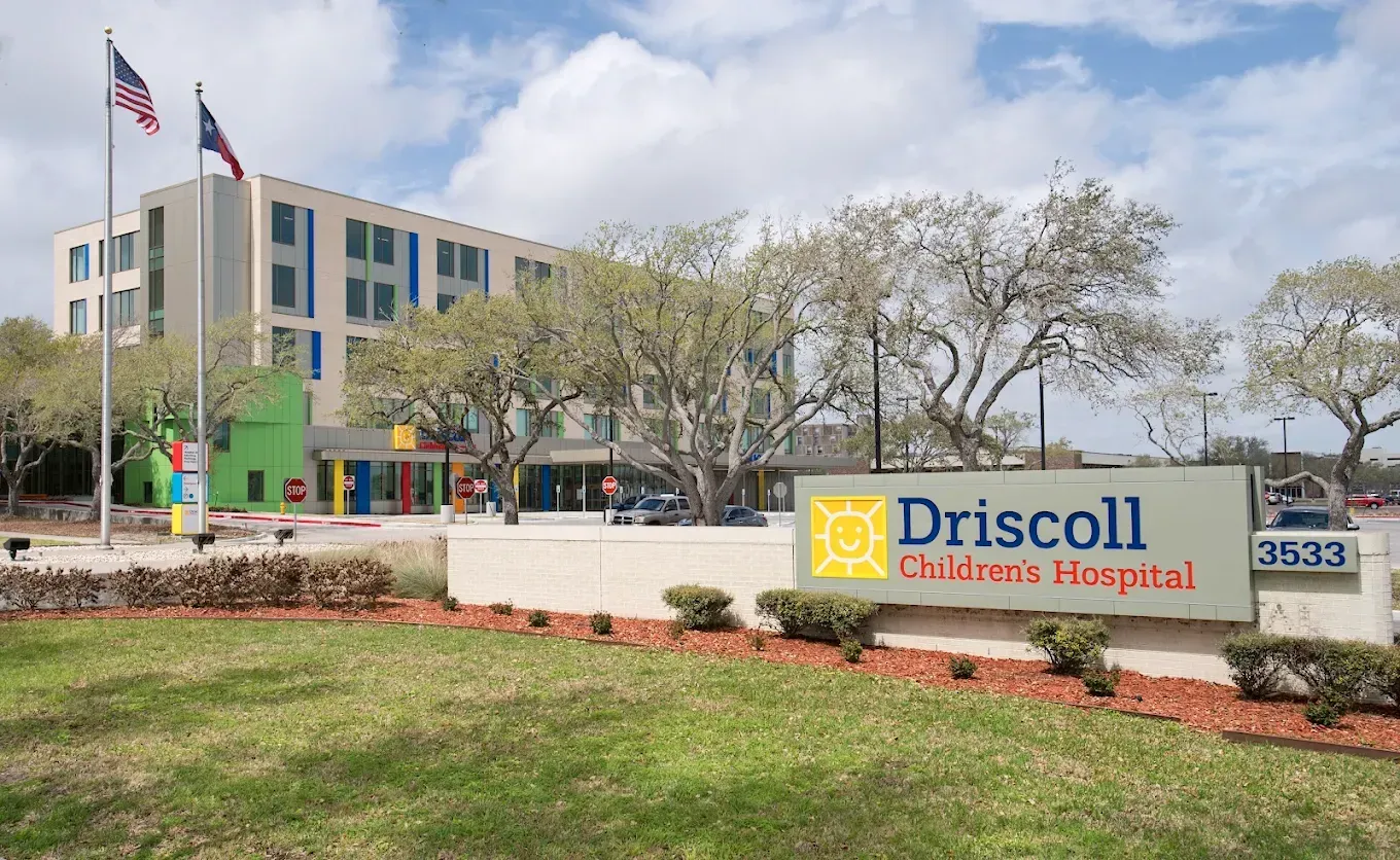 Driscoll Children's Hospital sign outside a modern hospital building with trees and flags
