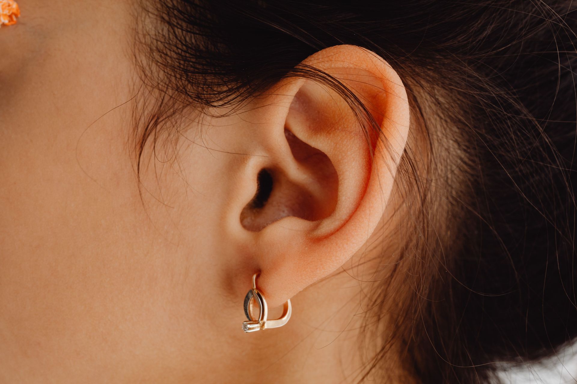 Close-up of an ear with a small silver hoop earring and dark hair pulled back