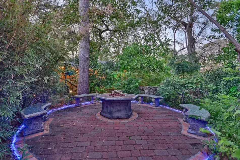 Brick patio with fire pit, surrounded by stone benches and lush greenery.