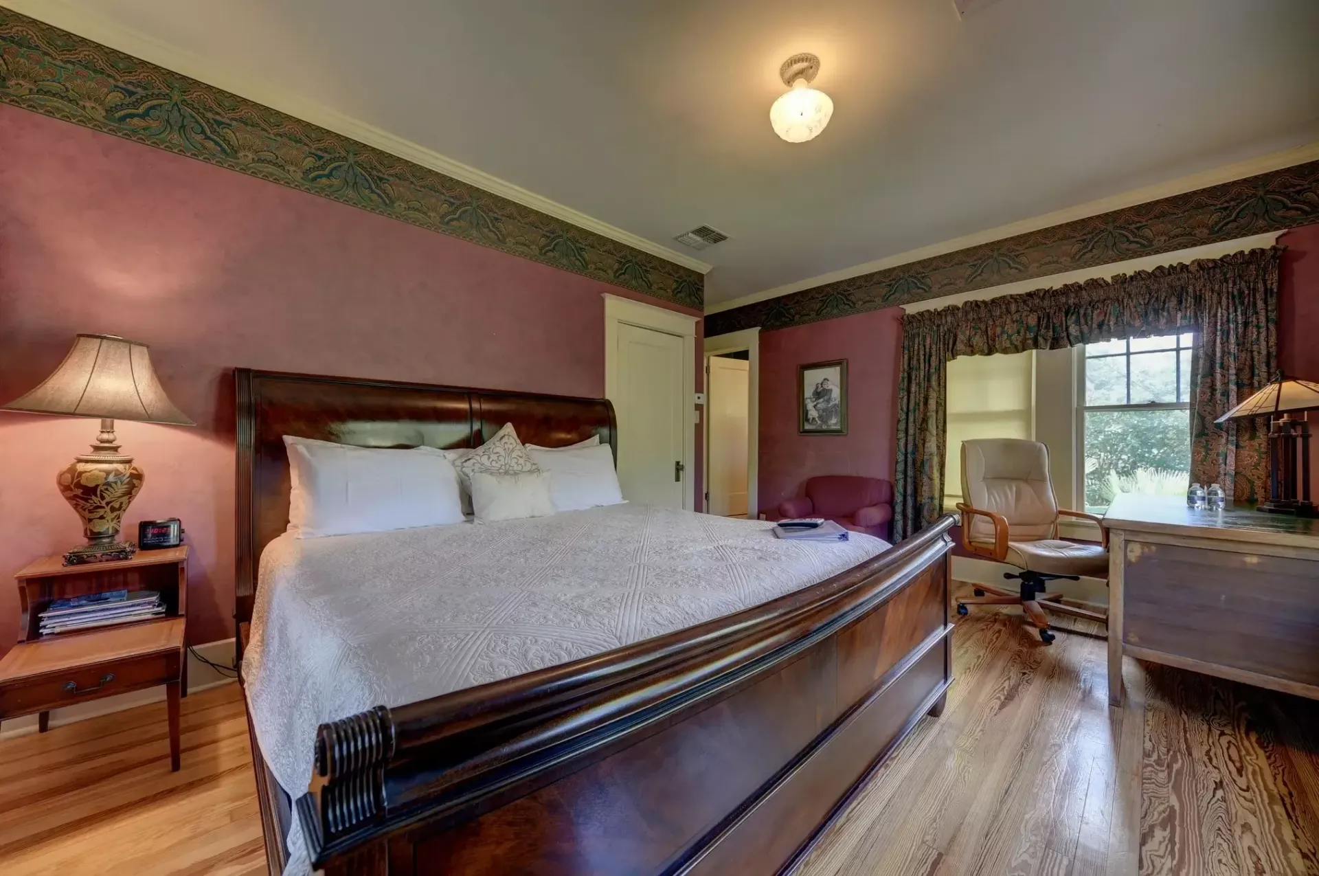 Bedroom with a dark wooden bed, pink walls, and a desk near the window.