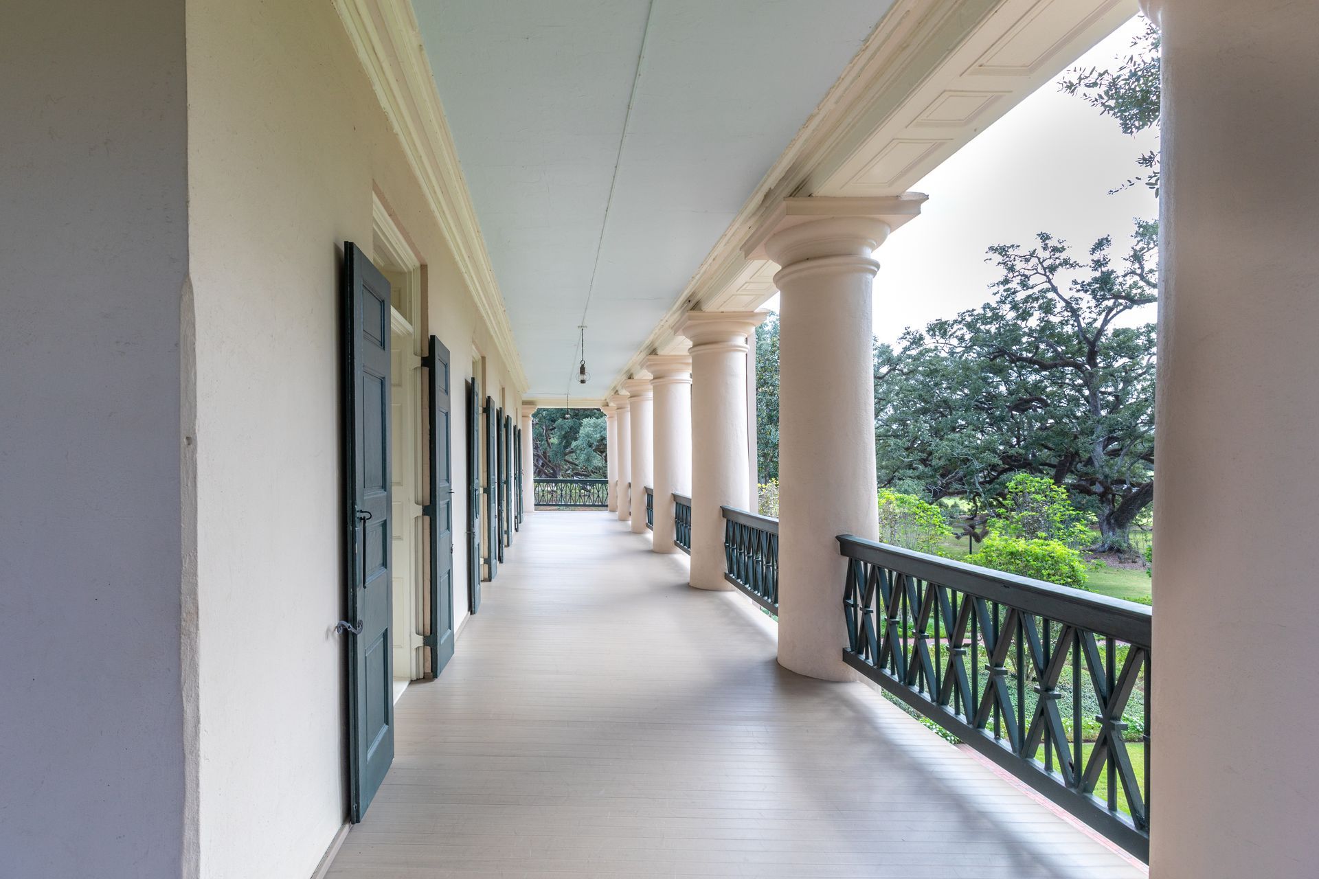 Covered porch with white columns, black railing, and doors along a cream-colored exterior hallway.