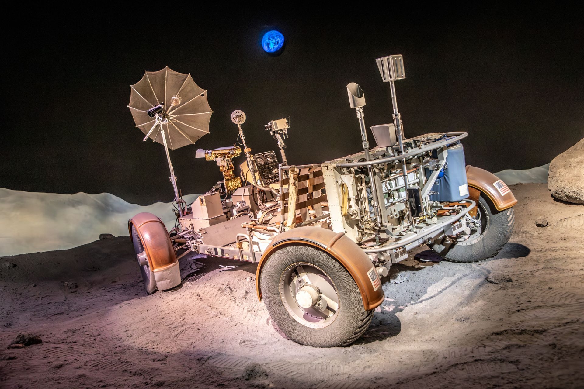 Moon rover on rocky terrain under a dark sky with a bright blue Earth in the background