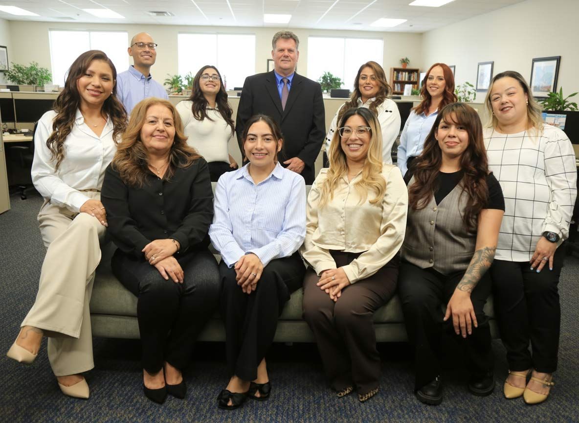 Office team posing together. People are seated and standing in an office with neutral colors.